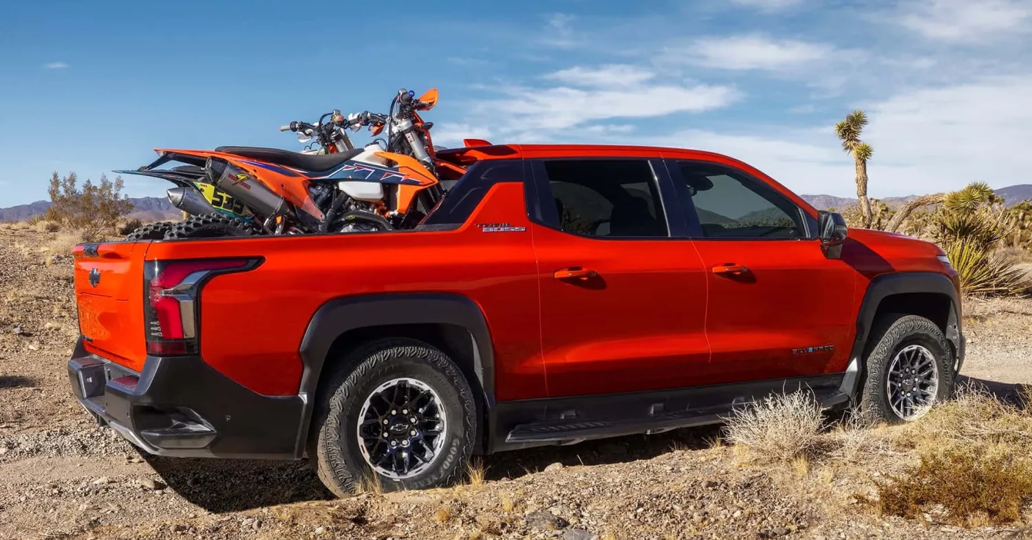 Silverado EV Trail Boss Red pickup truck carrying two dirt bikes outdoors